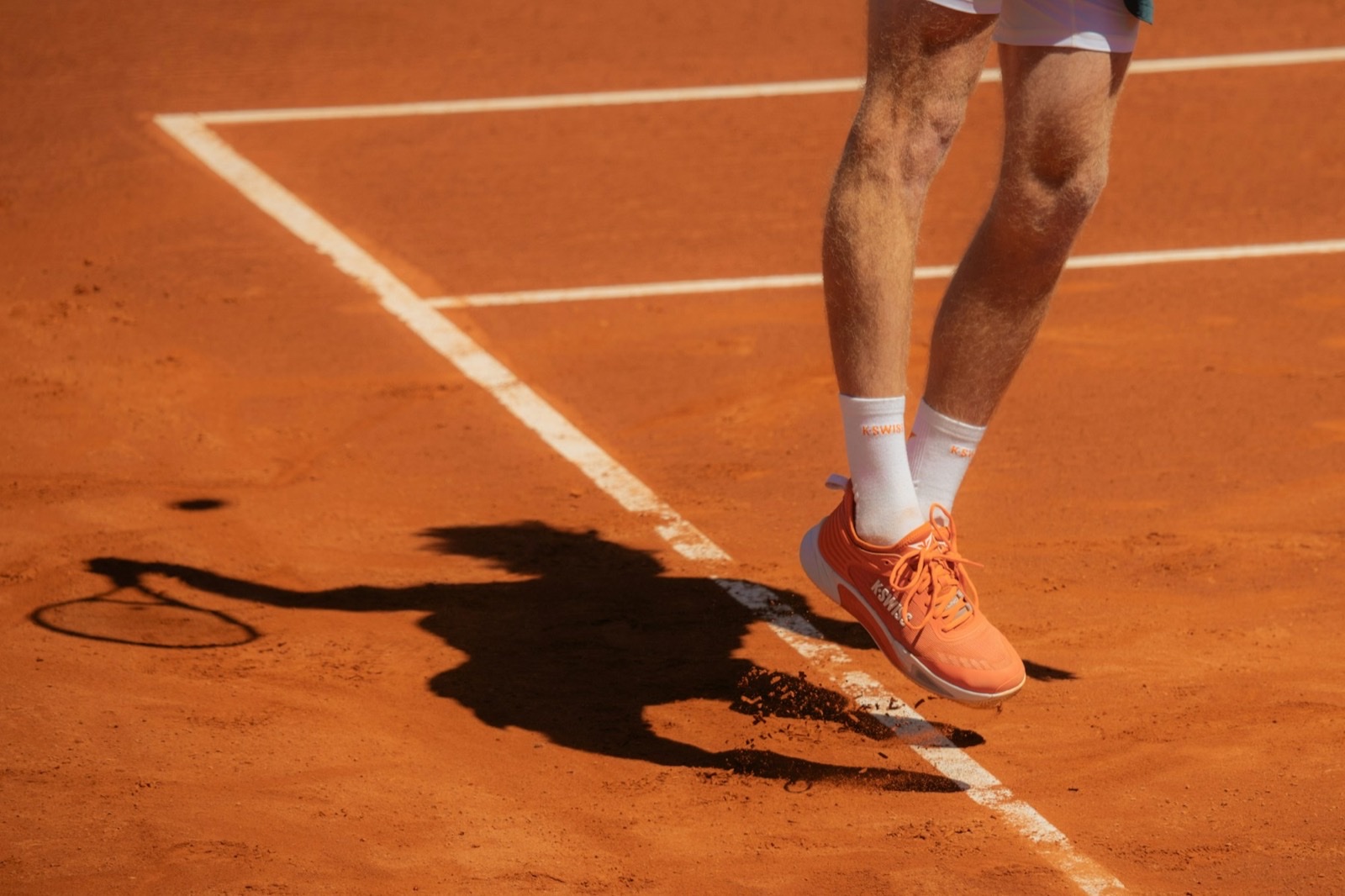 A tennis player’s feet on clay, shadow of the swing